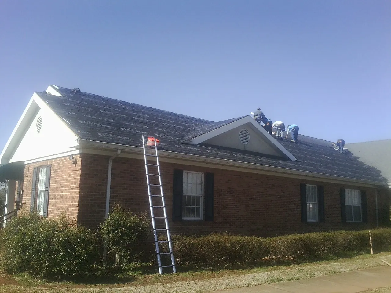 Crew tearing shingles off a brick ranch roof with a ladder set — Emergency Roof Repair work by our crew in Yalaha