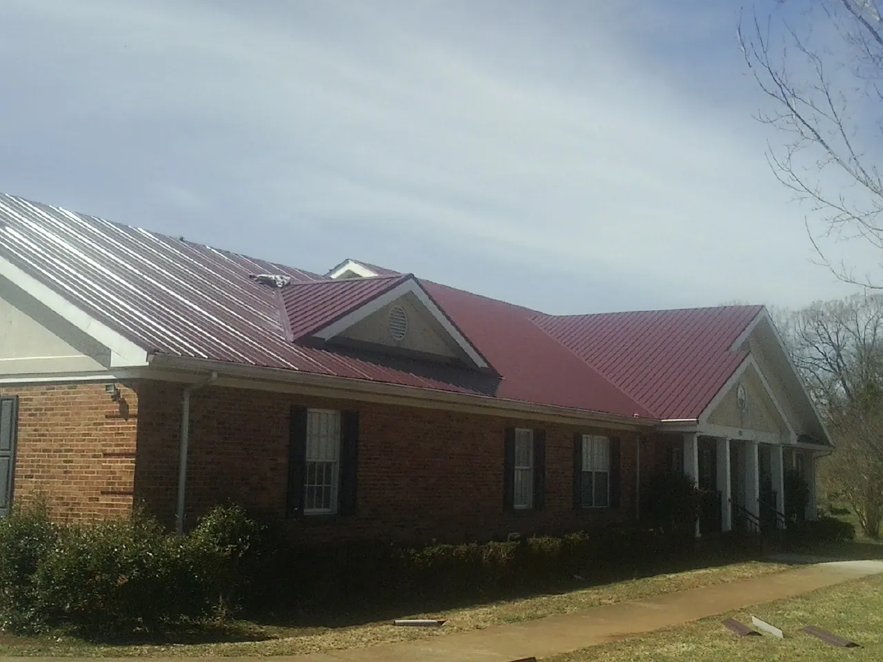 Red metal roof with gabled entries on a long brick building, from a Hail Damage Roof Repair job in Yalaha