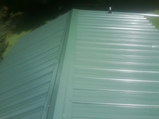 New green metal panels meeting at the ridge of a roof — Flat Roof Repair work by our crew in Yalaha