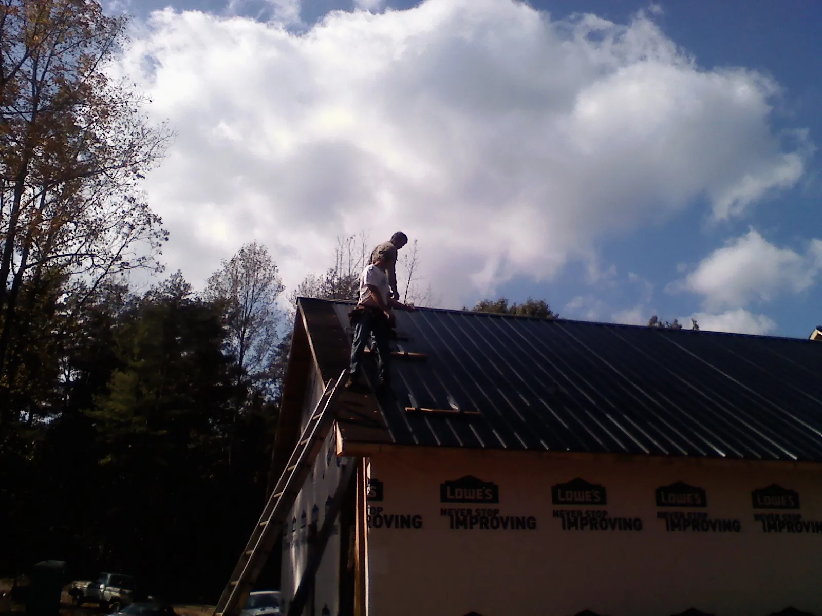 Roofer fastening dark metal panels high against a cloudy sky, from a Roof Inspection job in Yalaha