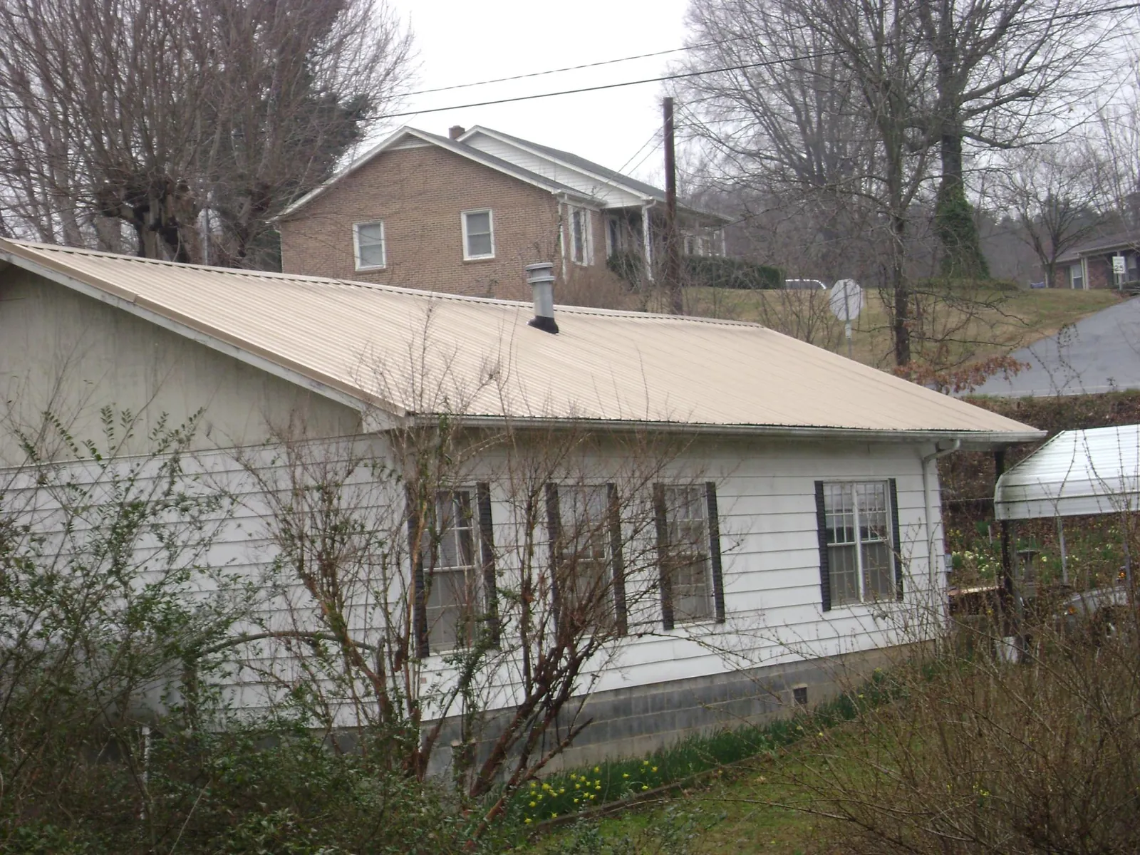 Tan metal roof on a white sided house set into a hillside — Commercial Roofing by Roofing Brothers in Yalaha